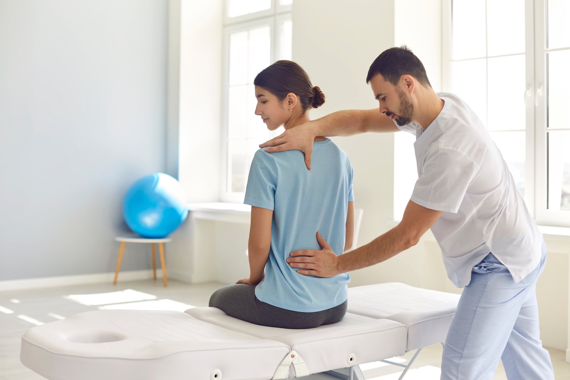 Licensed Osteopath Examining Young Female Patient's Back in Modern Hospital Office